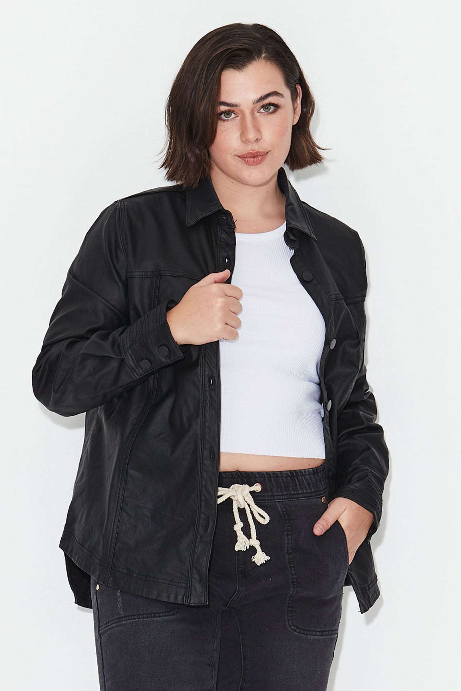 Model wears plus size black shacket with button front, shirt collar and long sleeves. Made from coated denim.