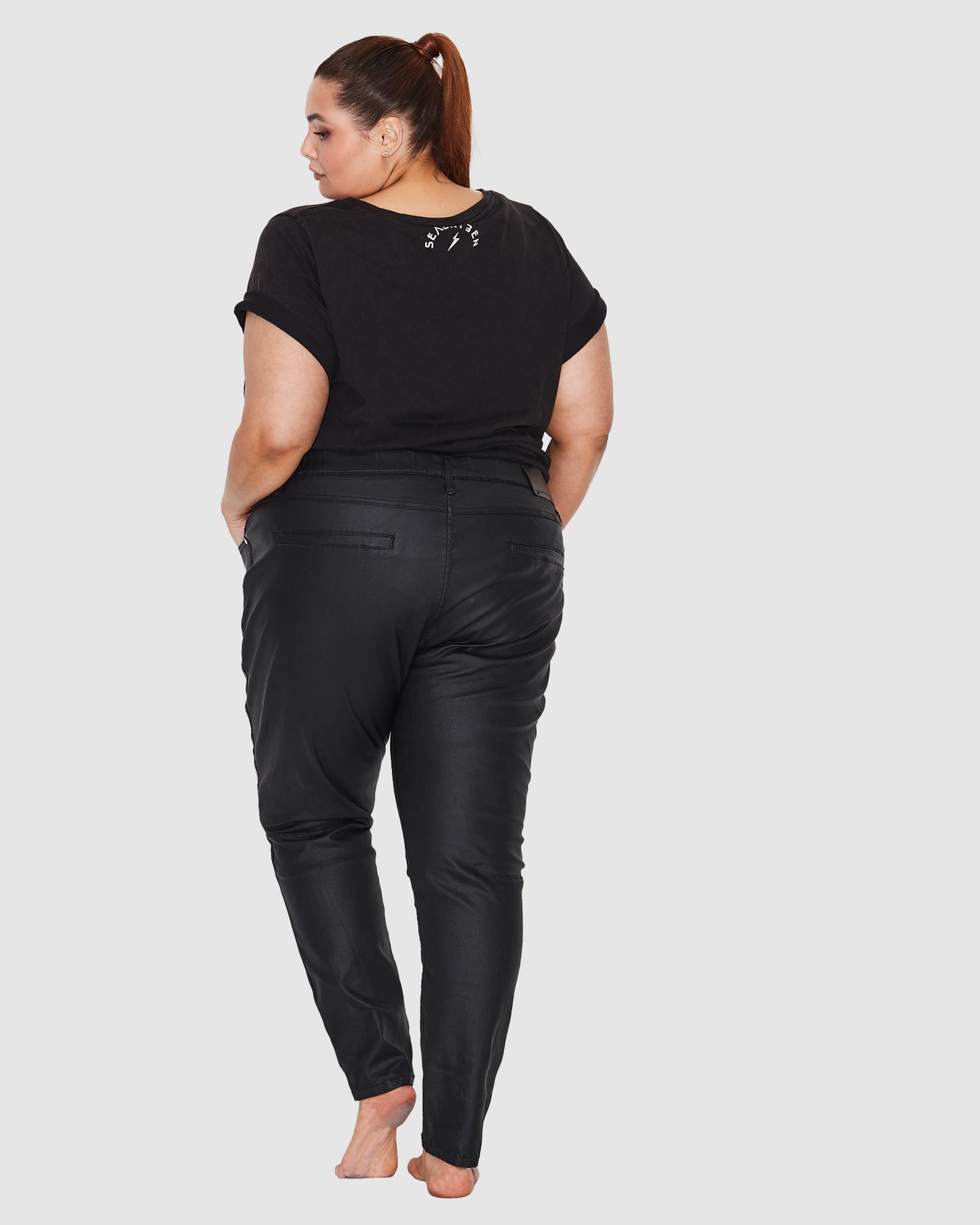 Back view of model wearing plus size black jeans made from coated denim 