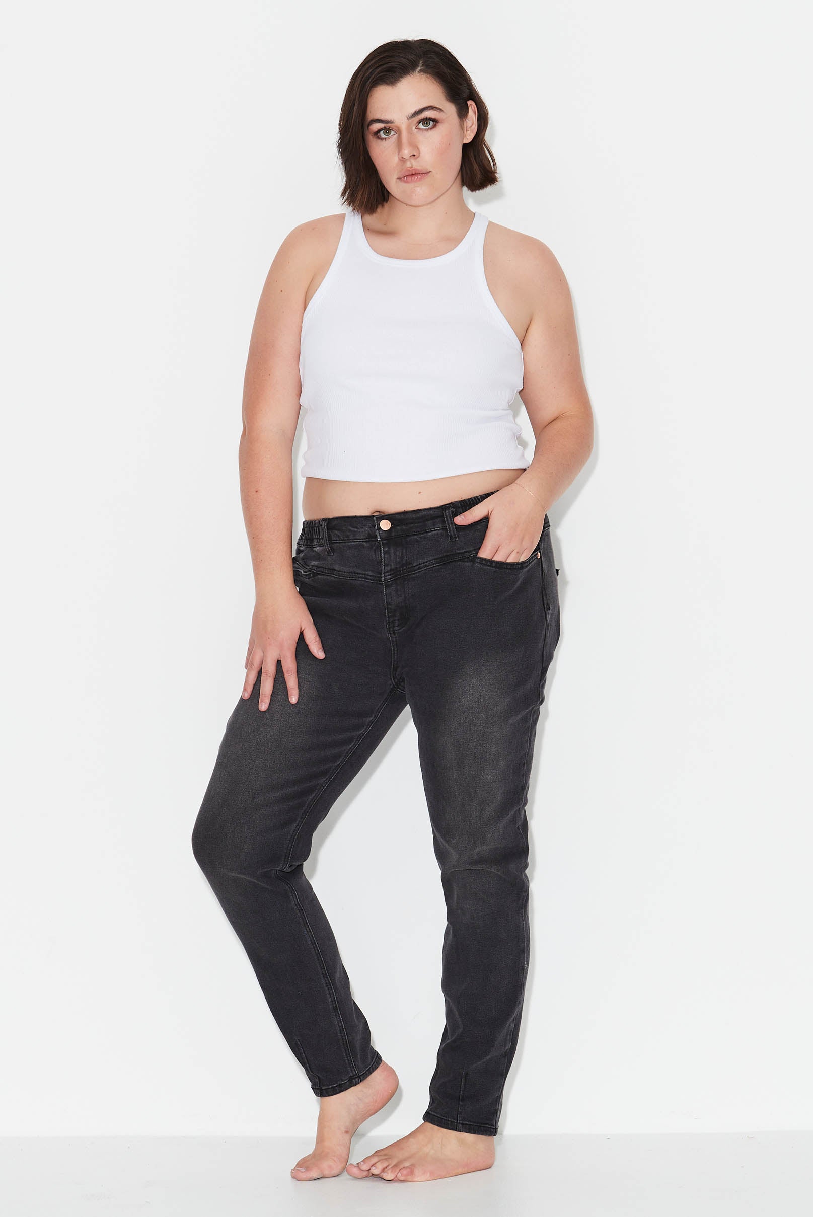 Model wears dark grey plus size jeans with tapered leg and yoke detail.